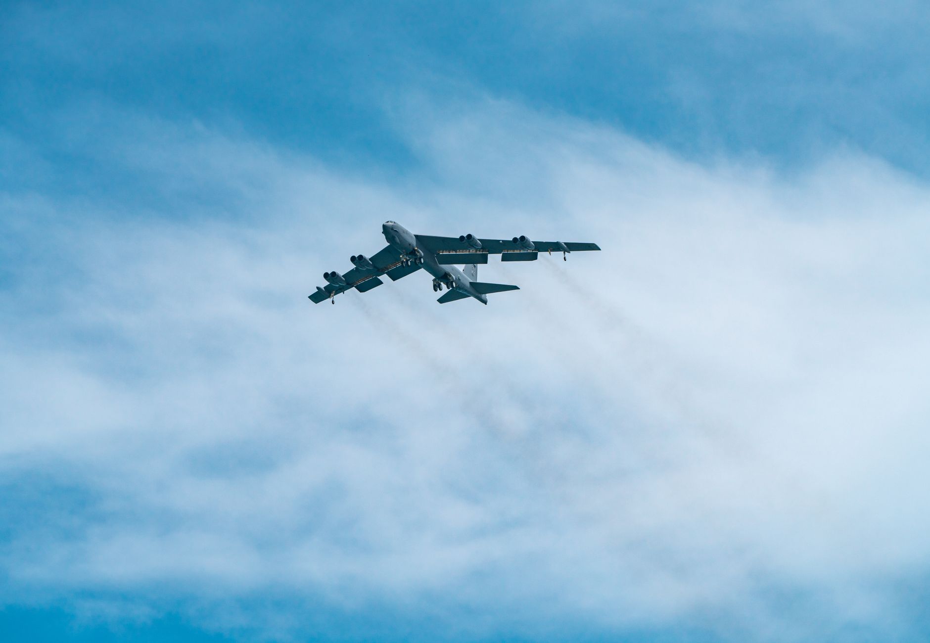 A B-52 Stratofortress aircraft soars through a clear blue sky on a sunny day.