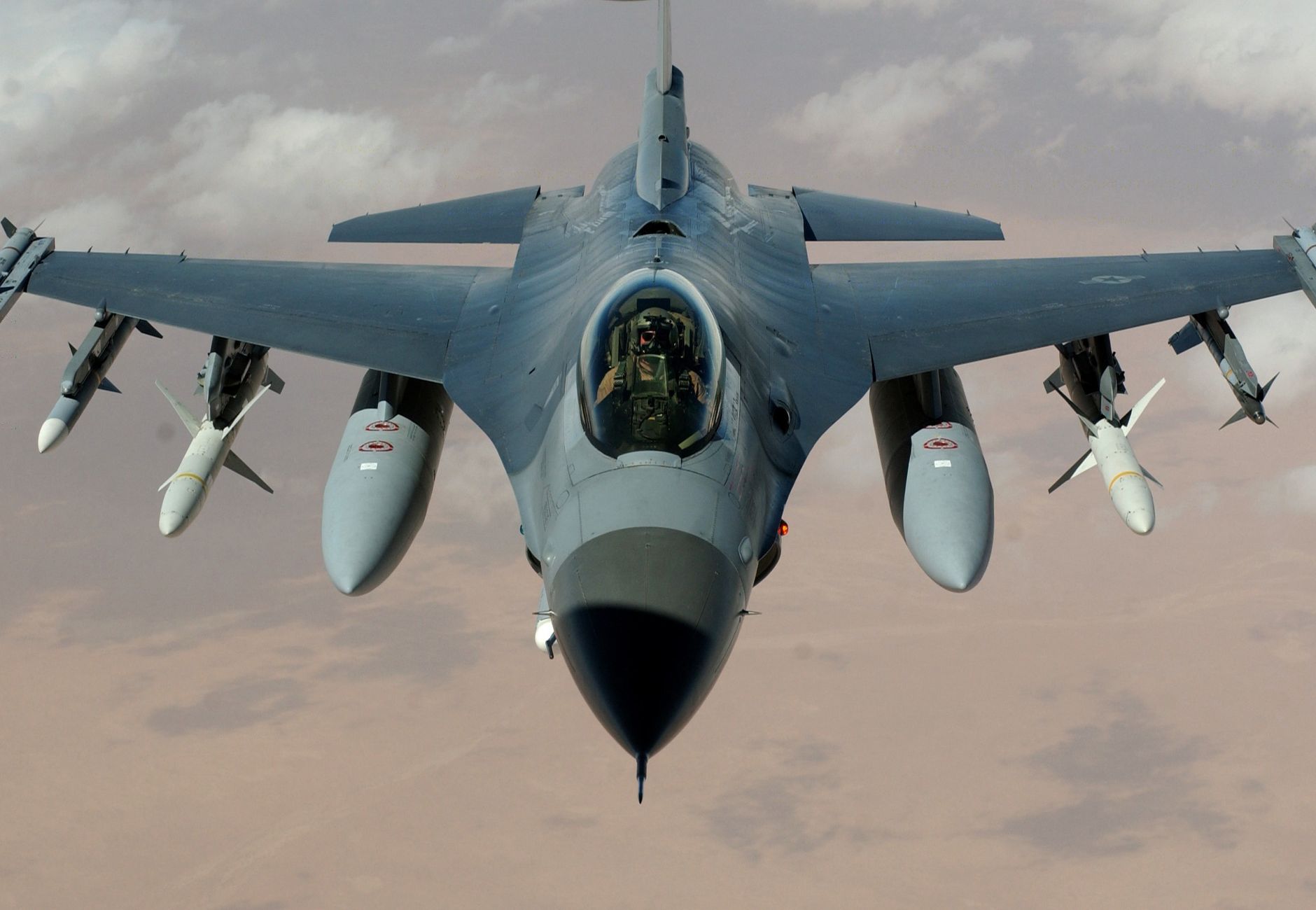 Powerful fighter jet soaring through clouds with visible missiles.