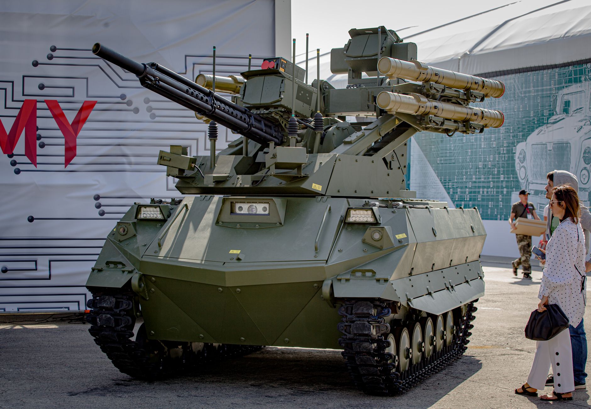 Green military tank with missile launchers on display outdoors with spectators.
