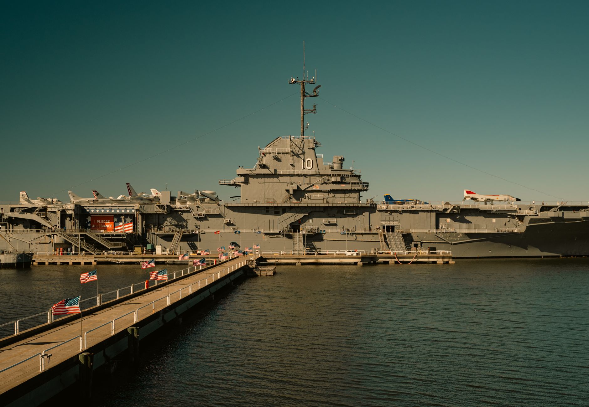 View of USS Yorktown aircraft carrier docked at harbor with walkway and flags.