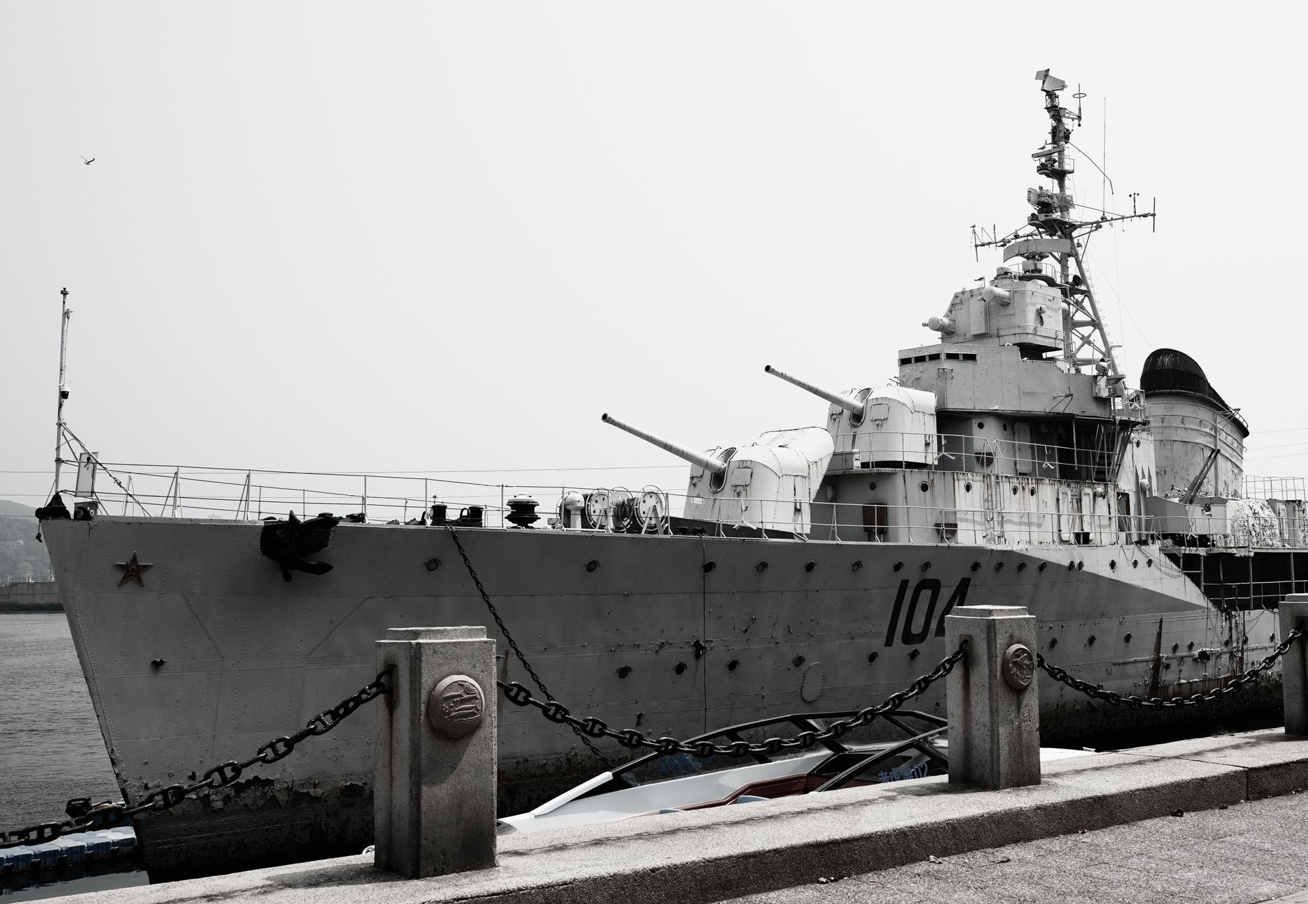 A large naval destroyer ship docked at a harbor under a gray sky.
