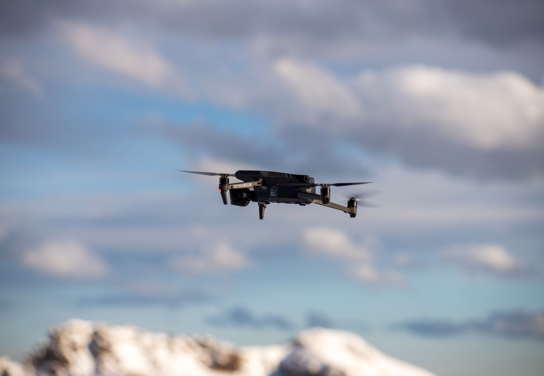 Aerial view of a drone flying over snow-covered mountains with dramatic clouds.