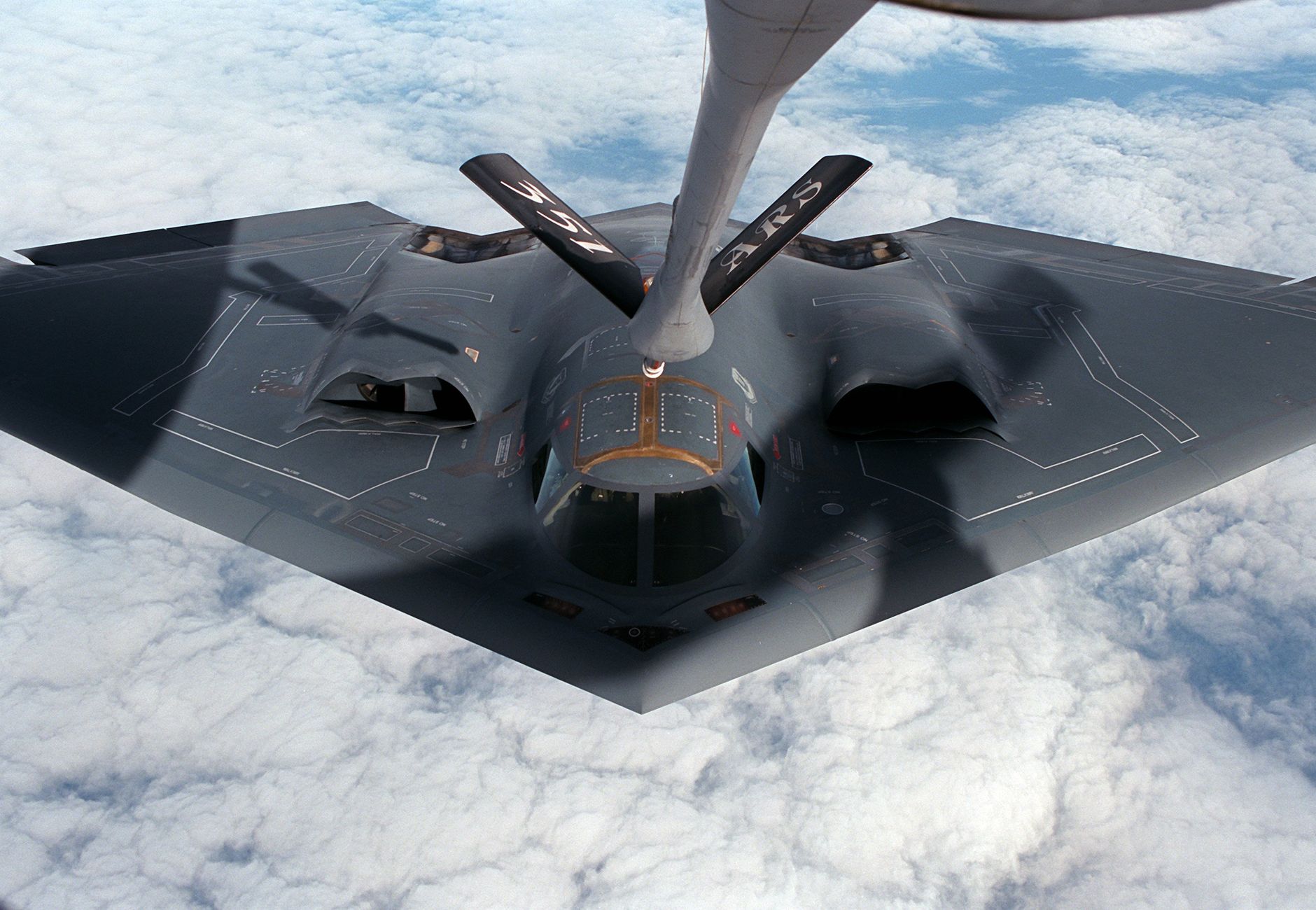 A stealth bomber aircraft receives aerial refueling mid-flight over clouds.