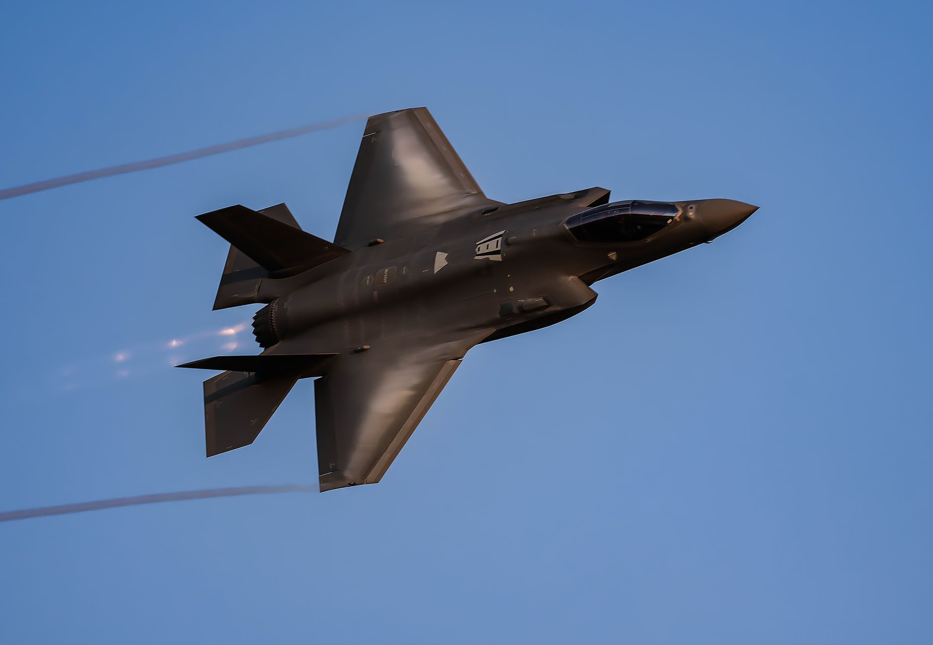 A sleek military fighter jet flying smoothly against a clear blue sky.
