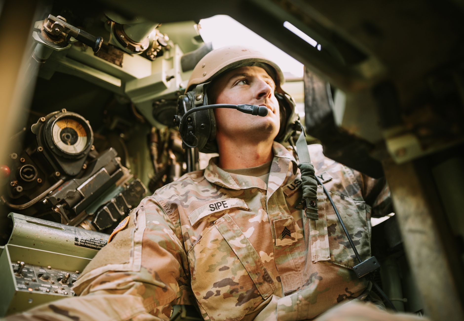A soldier in camouflage uniform inside an armored vehicle, looking focused.